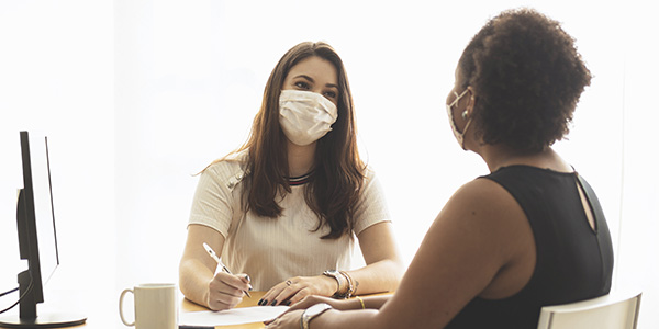 two women in an office at a job interview, wearing masks